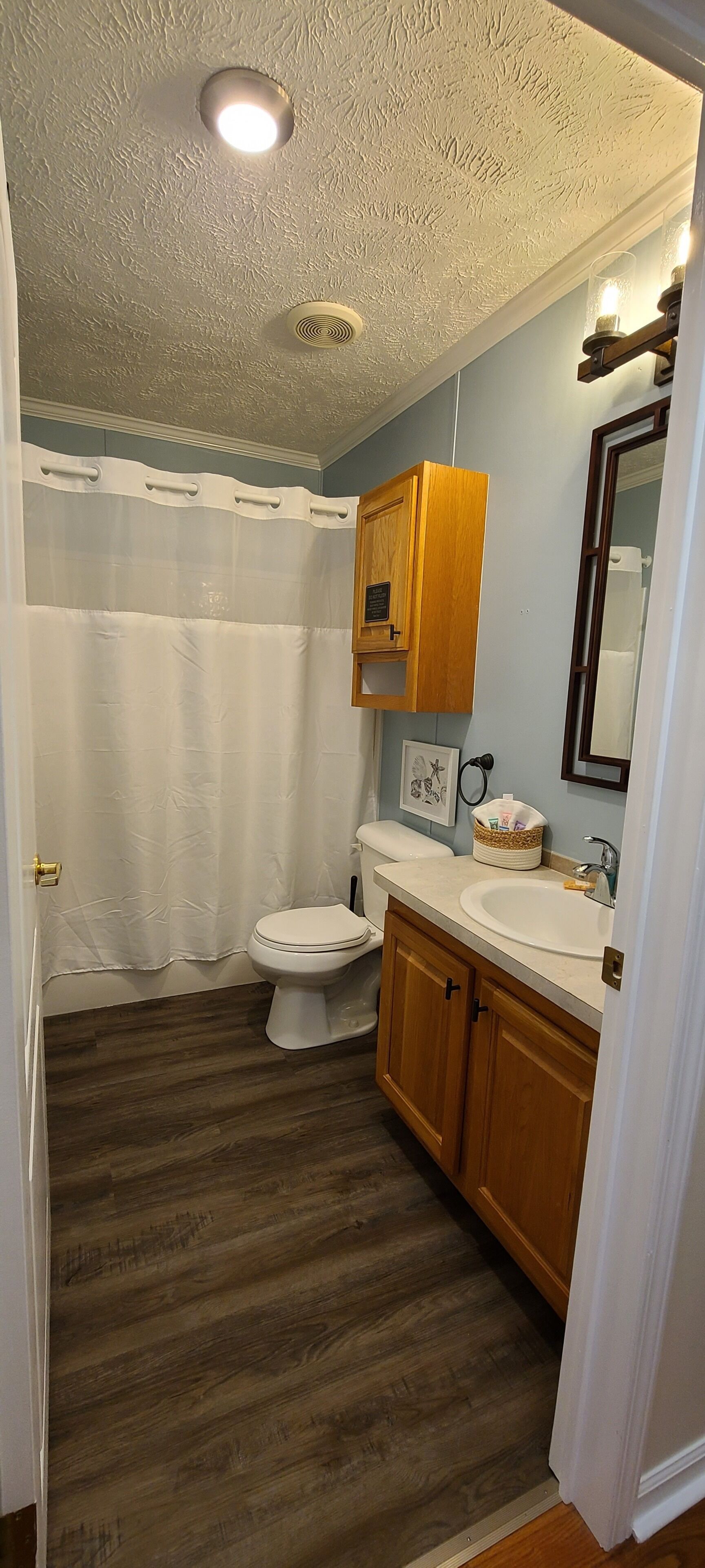Une salle de bain équipée d’un WC, d’un lavabo, de meubles en bois, d’un rideau de douche et d’un luminaire au plafond.