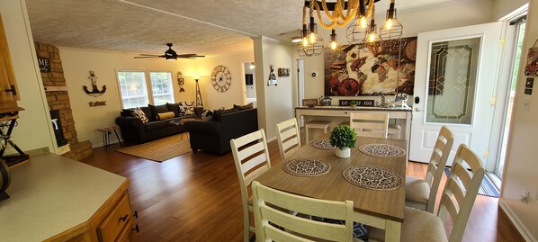 Uma sala de estar ampla com sofá, mesa de jantar com cadeiras, área de cozinha e ventilador de teto.