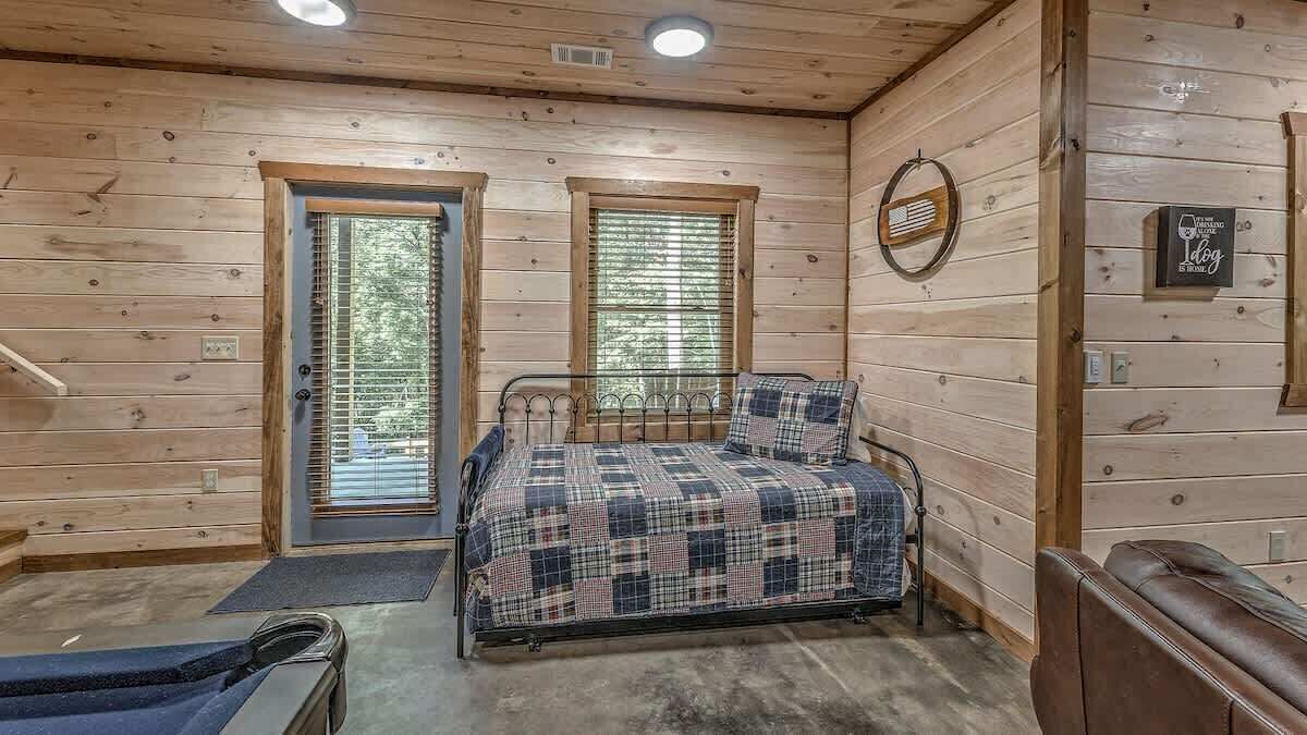 Una habitación de cabaña de madera con cama, un banco, una puerta y una ventana.