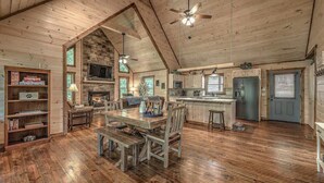 A rustic cabin interior with a dining area, kitchen, and living space, featuring wooden floors and a stone fireplace. - Take a Paws - close to downtown, fenced yard, pets (Blue Ridge)