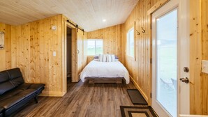 A wooden cabin bedroom with a bed, a black leather sofa, and a door leading to a balcony.