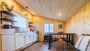 A cozy cabin interior with wooden walls, a kitchenette, a dining area, and a sofa.