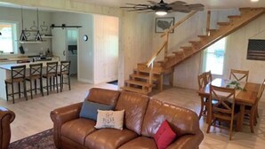 A spacious living area with a brown leather sofa, wooden dining table, and a staircase leading to an upper level.