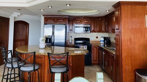A kitchen with wooden cabinets, a granite countertop, a stainless steel refrigerator, a black stove, and a microwave.