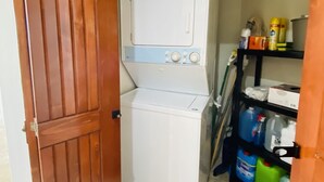 A laundry room with a washing machine and dryer, a wooden door, and shelves with cleaning supplies.