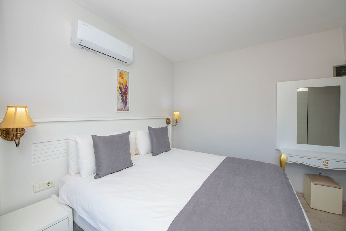 A hotel room with a bed, bedside lamps, an air conditioner, a television, and a small cabinet.