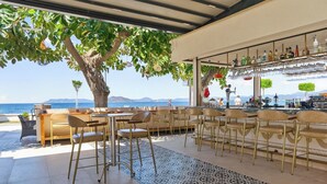 An outdoor seating area with tables and chairs, a bar with shelves of bottles, and a view of the sea. - Mia Casa Hotel (Fethiye)
