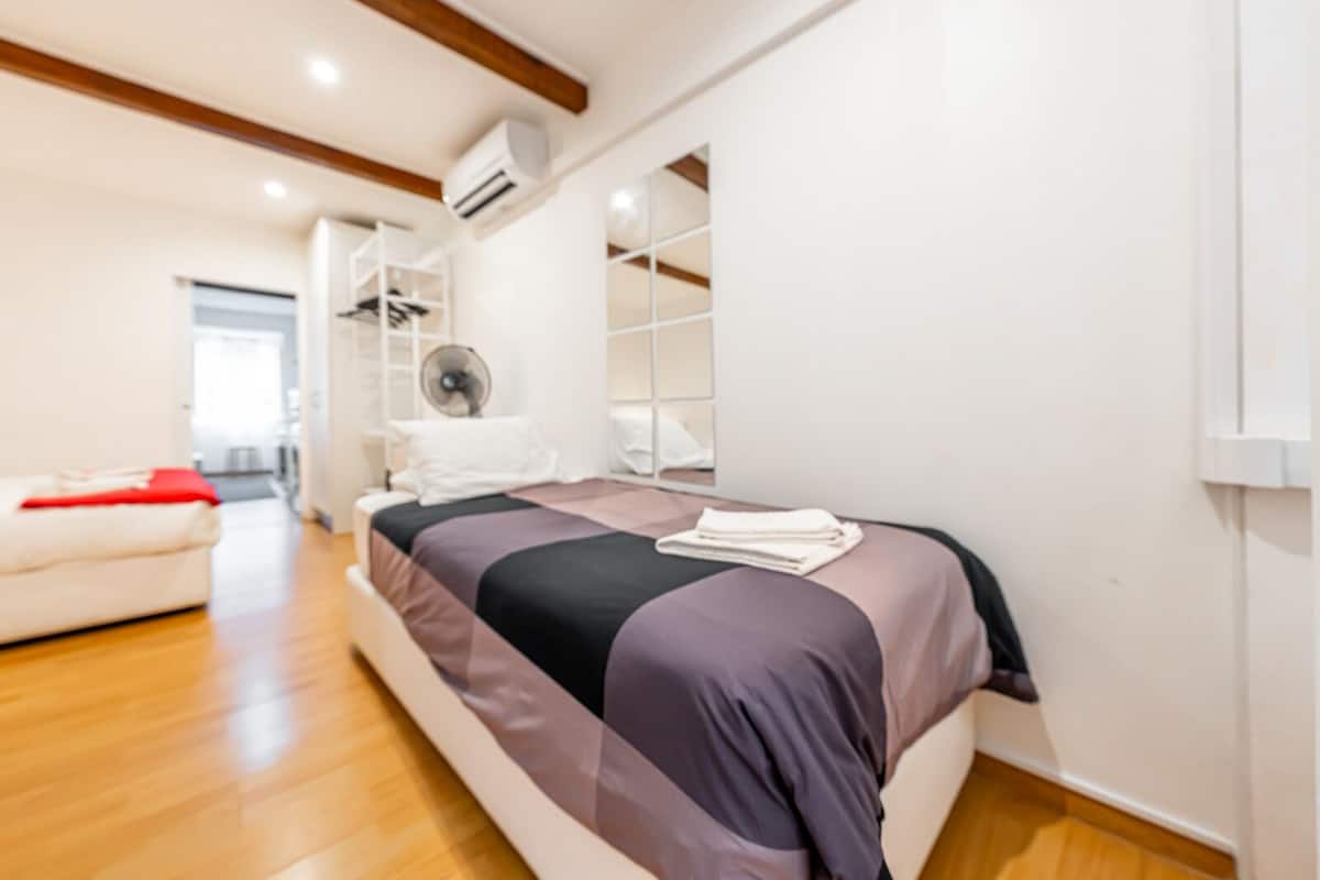 Une chambre à coucher moderne avec un lit, un ventilateur et une armoire blanche.