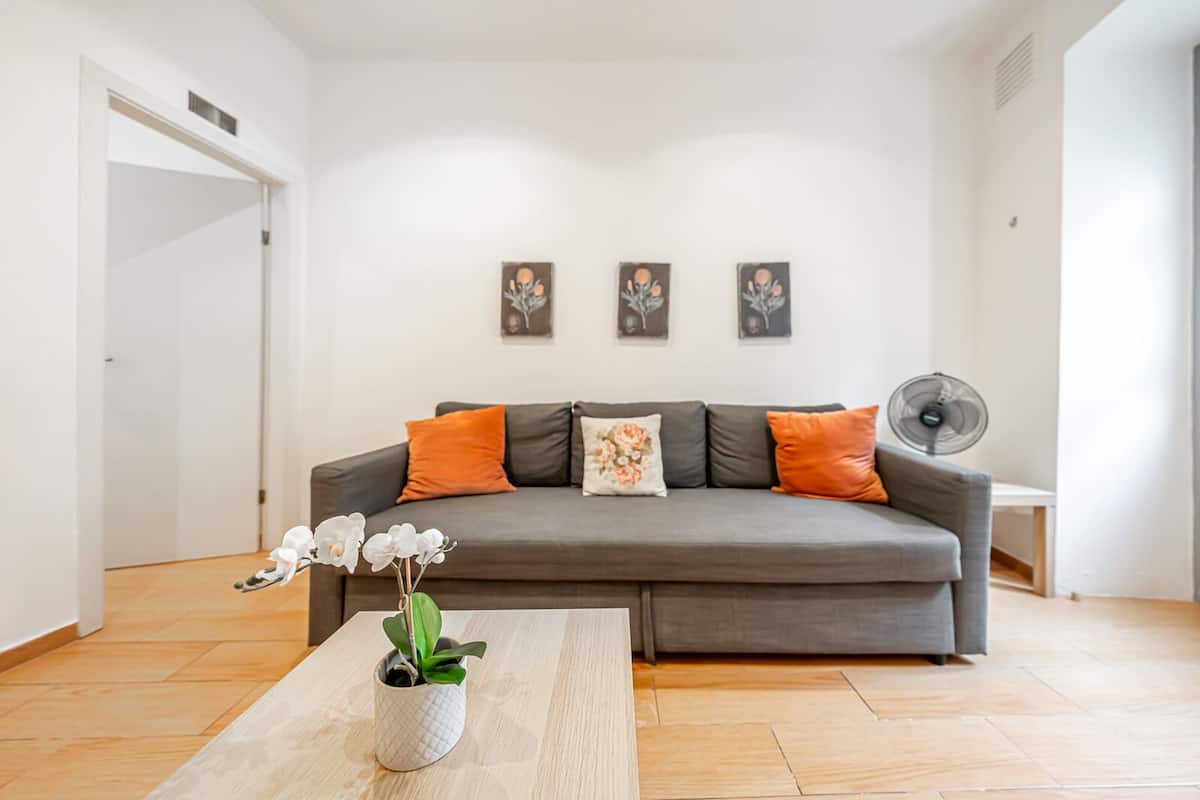 Un salon moderne avec un canapé gris, des coussins orange et une petite table sur laquelle est posée une plante.