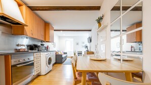 Une cuisine moderne avec des meubles en bois, un four encastré et un lave-linge. On y trouve également un coin repas avec une table et des chaises en bois.