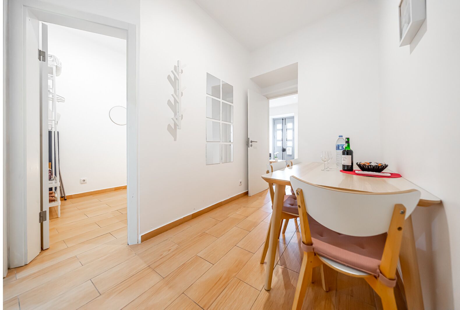 Ein moderner, minimalistischer Essbereich mit einem runden Tisch, Holzstühlen, einer weißen Wand mit Fenster und einer Tür zu einem anderen Raum.