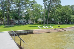 Uma piscina com um deck e espreguiçadeiras, rodeada por árvores e uma área gramada com um parquinho.