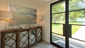 A room with a large window, a painting on the wall, and a console table with lamps and decorative items. - Stunning Five Bedroom Escape - Great Water! (Enchanted Oaks)