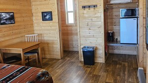 A cozy cabin with a wooden interior, a dining area, a kitchen with a microwave, and a ceiling fan. - Canyons of Escalante RV Park (Escalante)