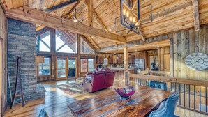 A spacious interior with a wooden ceiling, large windows, a dining area with a wooden table, and a kitchen with wooden cabinets. - Rustic Sunsets - Mountain Views, Hot tub, Arcade, Pool, Central, Aska Adventure (Blue Ridge)