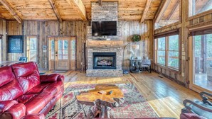 A log cabin interior with a stone fireplace, leather sofa, and large windows. - Rustic Sunsets - Mountain Views, Hot tub, Arcade, Pool, Central, Aska Adventure (Blue Ridge)