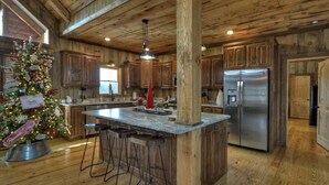 A kitchen with wooden cabinets, a stainless steel refrigerator, a marble island with stools, and a Christmas tree. - Rustic Sunsets - Mountain Views, Hot tub, Arcade, Pool, Central, Aska Adventure (Blue Ridge)