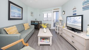 A living room with a sofa, coffee table, TV, and a ceiling fan. - Beachfront Condo, sleeps 6, pools, hot tub, tiki bar, golf carts allowed (Myrtle Beach)