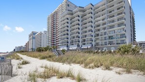 A multi-story hotel with balconies, located near a sandy beach area. - Beachfront Condo, sleeps 6, pools, hot tub, tiki bar, golf carts allowed (Myrtle Beach)