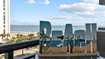 A wooden sign with the word "REACH" and beach-themed decorations, overlooking a beach with palm trees and a lighthouse.