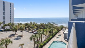A high-rise hotel with a view of the ocean, a parking lot, and a pool area. - Beachfront Condo, sleeps 6, pools, hot tub, tiki bar, golf carts allowed (Myrtle Beach)