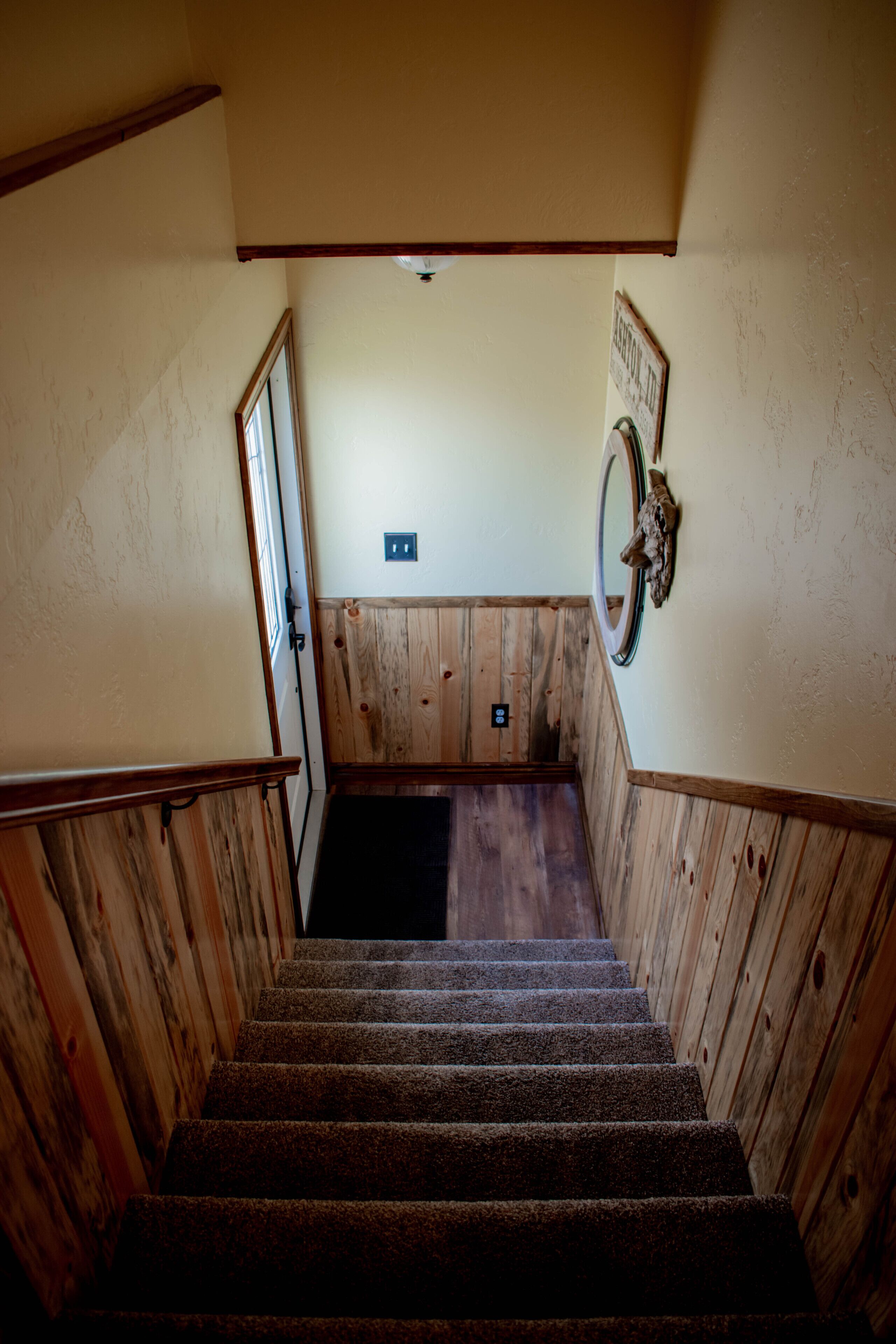 A wooden staircase with a carpeted landing, a wall-mounted light fixture, and a framed sign.
