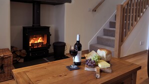 Un salon chaleureux avec un poêle à bois, une table en bois sur laquelle se trouvent une bouteille de vin, un verre, du pain et du fromage.