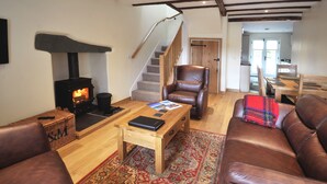 Un salon chaleureux avec une cheminée, des meubles en cuir, une table basse en bois et un escalier menant à une autre pièce.