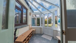 Ein Wintergarten mit einer hölzernen Bank, einem Tisch und Blick ins Freie.