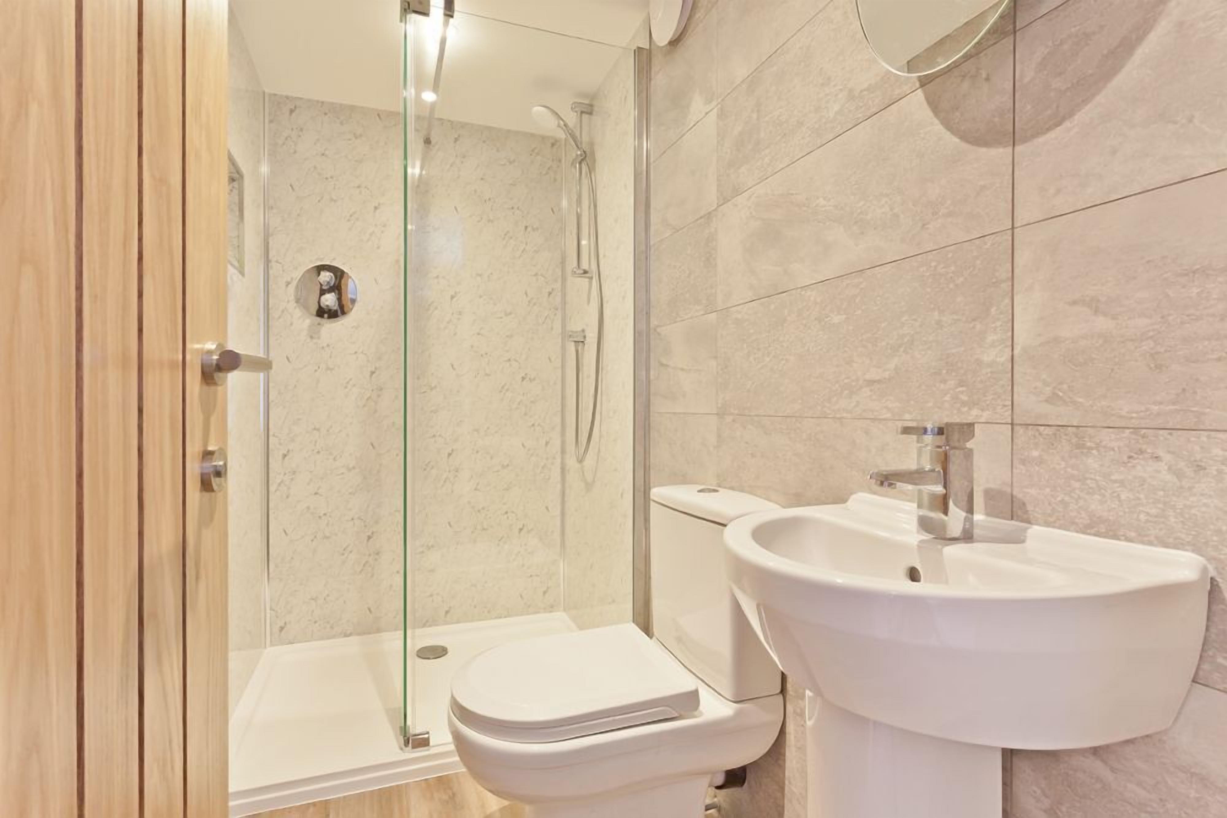 Et moderne badeværelse med et glasafskærmet brusebad, et hvidt toilet og en vægmonteret vask.
