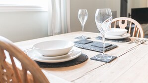 Een eettafel gedekt met witte borden, twee wijnglazen en zwarte onderzetters.