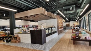 Un espace de vente moderne où une variété de produits sont présentés sur des étagères et des tables, avec un sol à carreaux et de grandes fenêtres le long d’un des murs.