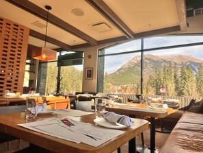 Un ristorante con tavoli apparecchiati, un menu sul tavolo e vista sulle montagne attraverso ampie finestre.