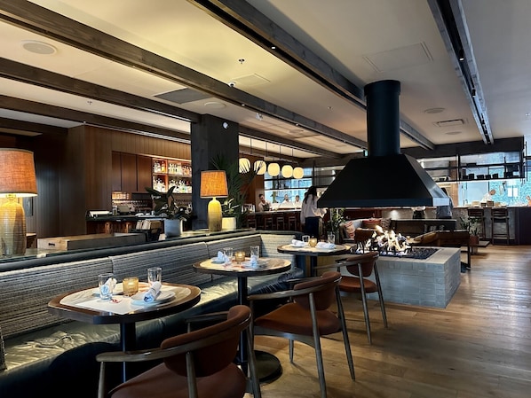 A modern restaurant with a bar area, wooden flooring, and a large black industrial-style light fixture.