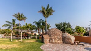 Un patio con una fuente de piedra, palmeras y un pérgola.
