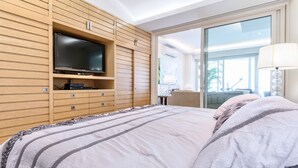 Un dormitorio moderno con una cama grande, televisor integrado y un ventanal corredero que da a un balcón.