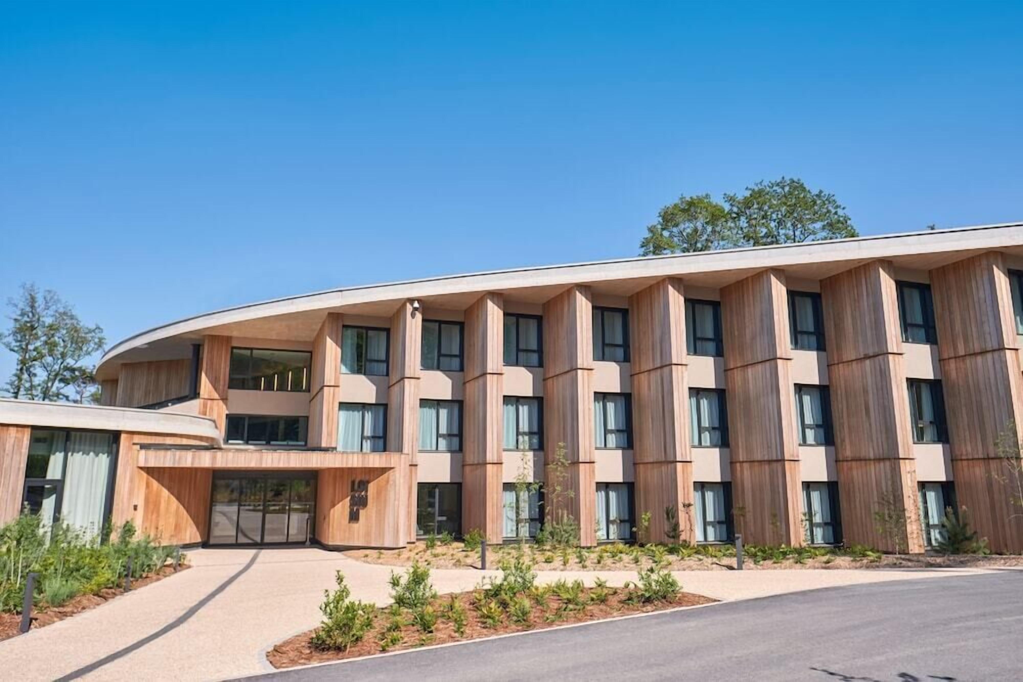 A modern building with a curved facade, large windows, and a landscaped entrance area.