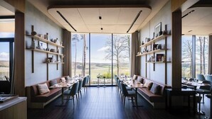 Un restaurante con una mesa larga y bancos, ventanas amplias y estantes con objetos.