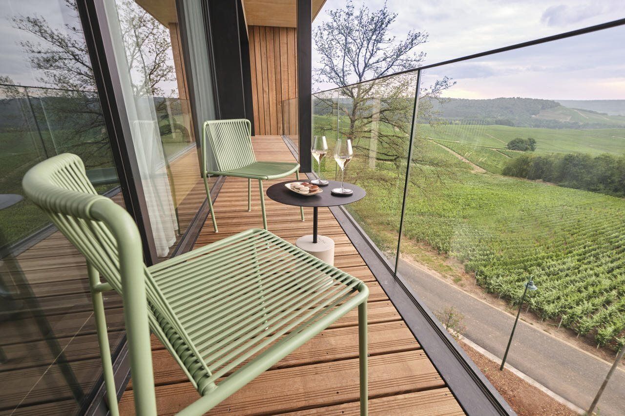 Un balcon avec une table et des chaises, une balustrade en verre et une vue sur un vignoble.