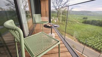Un balcon avec une table et des chaises, une balustrade en verre et une vue sur un vignoble.