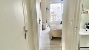 Ein schmaler Flur führt zu einem Schlafzimmer mit Bett und Fenster.