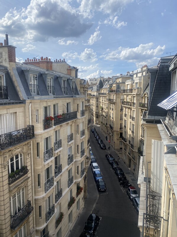 A narrow street flanked by multi-story buildings with balconies and parked cars.