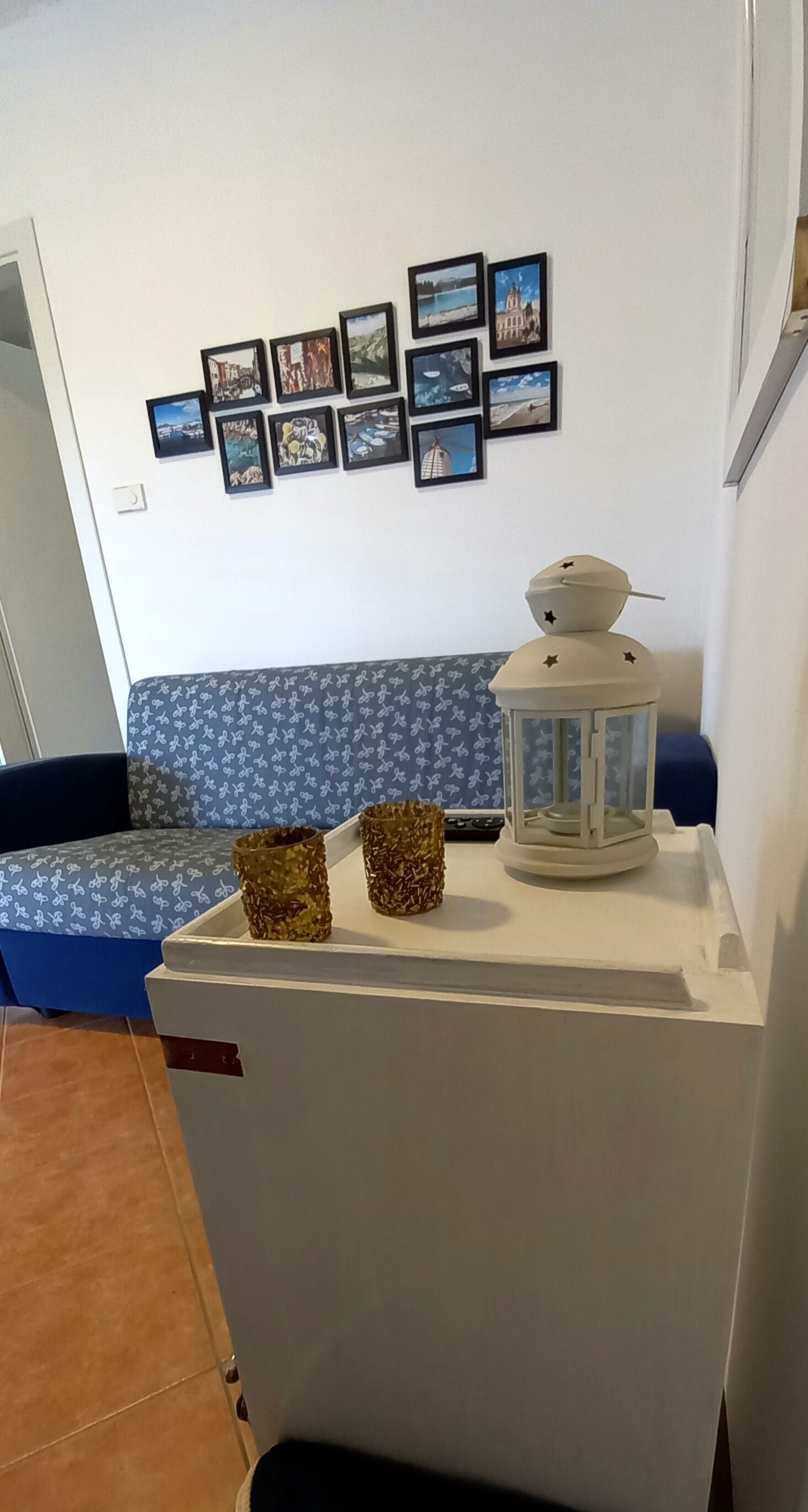 A corner of a room with a white cabinet, a blue patterned sofa, and a wall decorated with framed pictures.