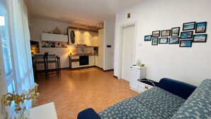 Ein Wohnzimmer mit einer Couch und einem Essbereich mit Tisch und Stühlen. Im Hintergrund befindet sich eine Küche.
