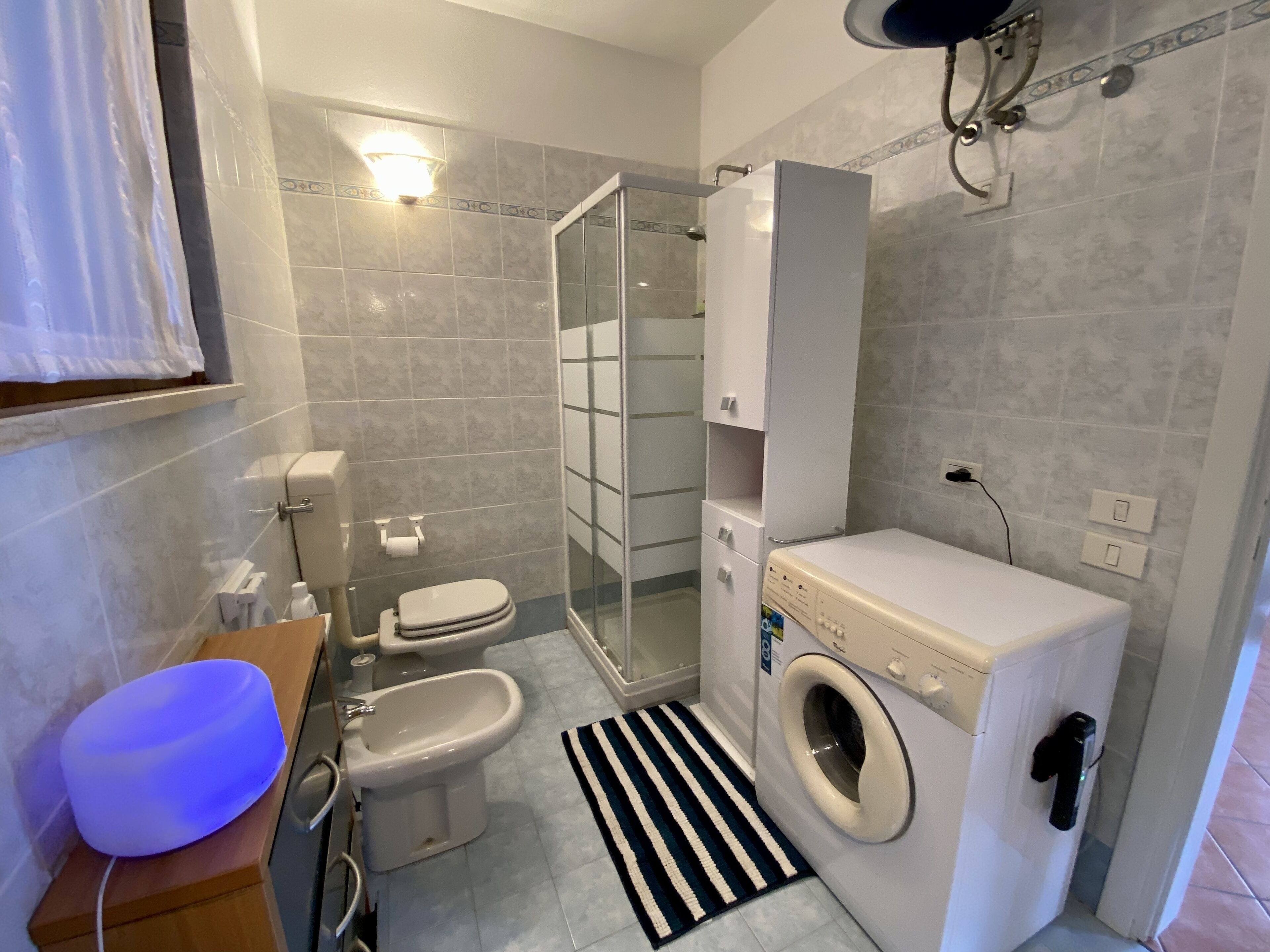 Ett modernt badrum med toalett, bidé, dusch och tvättmaskin.