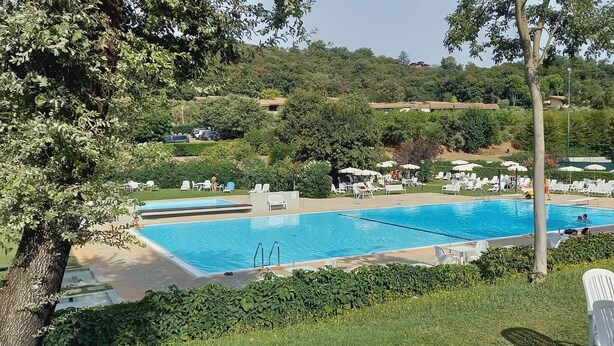Ein rechteckiger Swimmingpool mit glasklar blauem Wasser, umgeben von weißen Liegestühlen und Sonnenschirmen, vor einer Kulisse aus üppiger Vegetation und Hügeln.