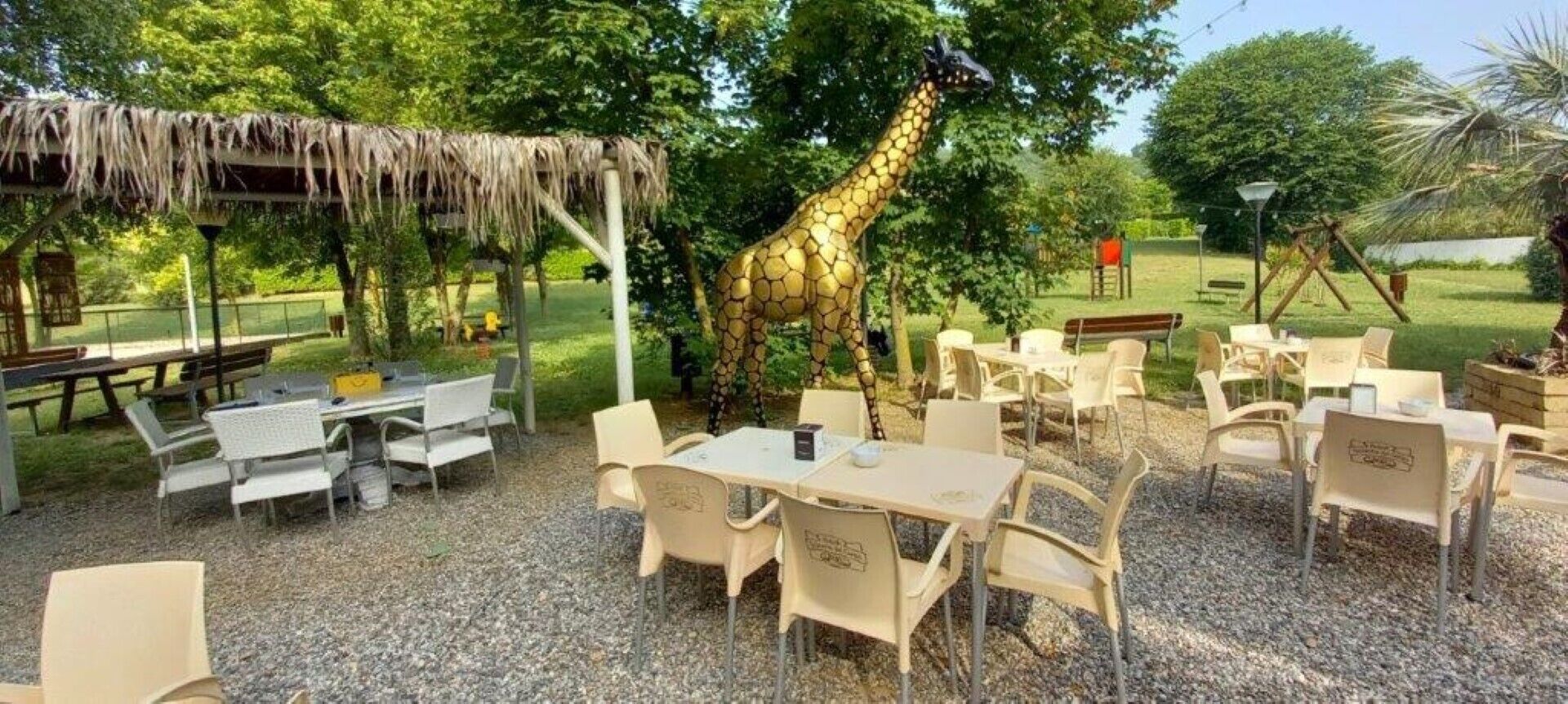 Een terras met tafels en stoelen, een rieten constructie en een girafbeeld.