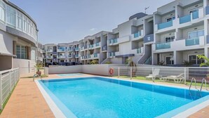 A modern apartment building with a swimming pool, balconies, and a clear sky.