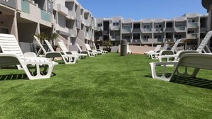 A hotel courtyard with white lounge chairs arranged in rows, a well-maintained lawn, and multi-story buildings in the background.