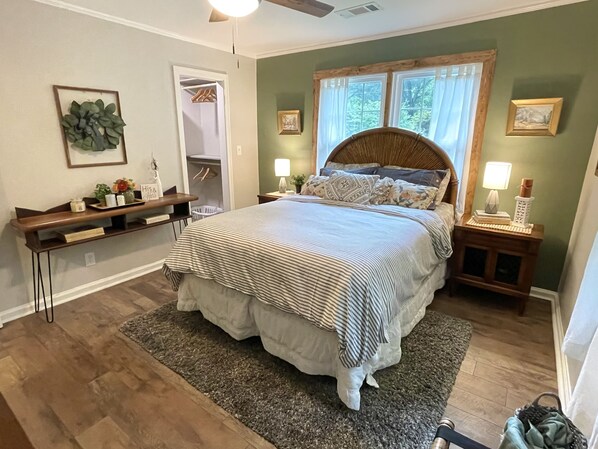 A bedroom with a bed, bedside tables, a nightstand, a dresser, a closet, and a window with curtains.